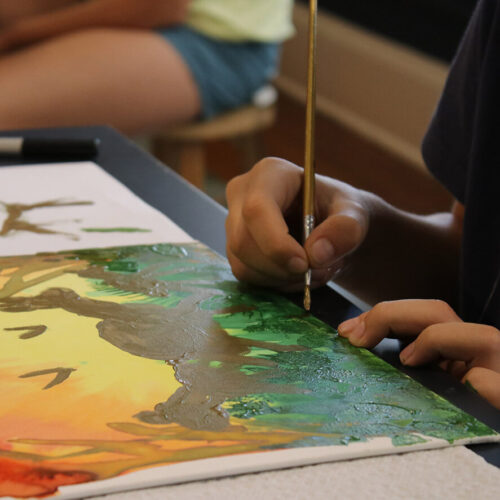 A close up shot of a student's hands paints a canvas.