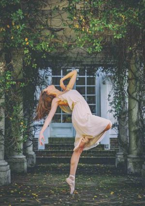 Phone of a Female ballet dancer dancing in front of a stone building covered in vines and flowers