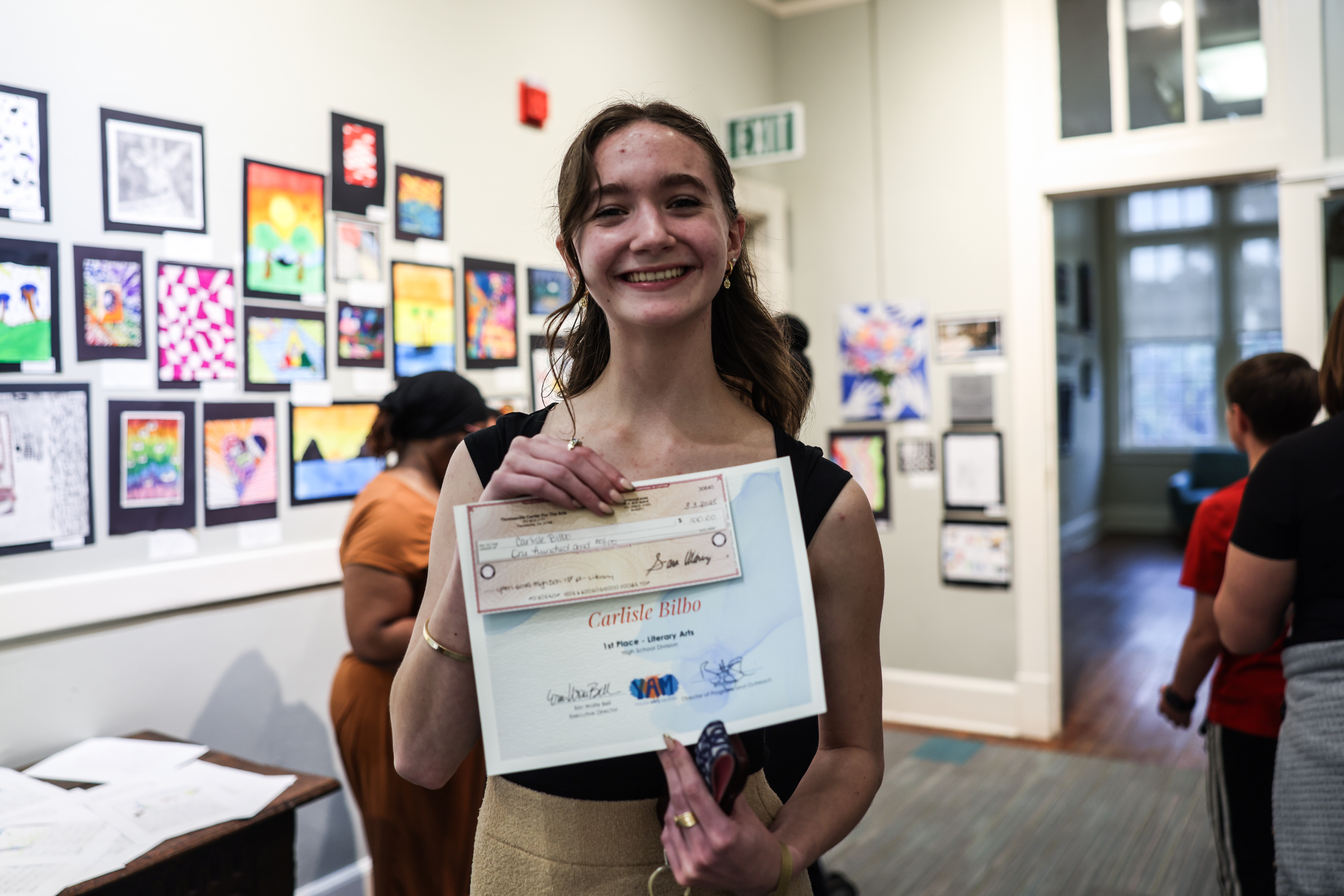 A student artist holding a certificate, recognized as a winner during Youth Arts Month.