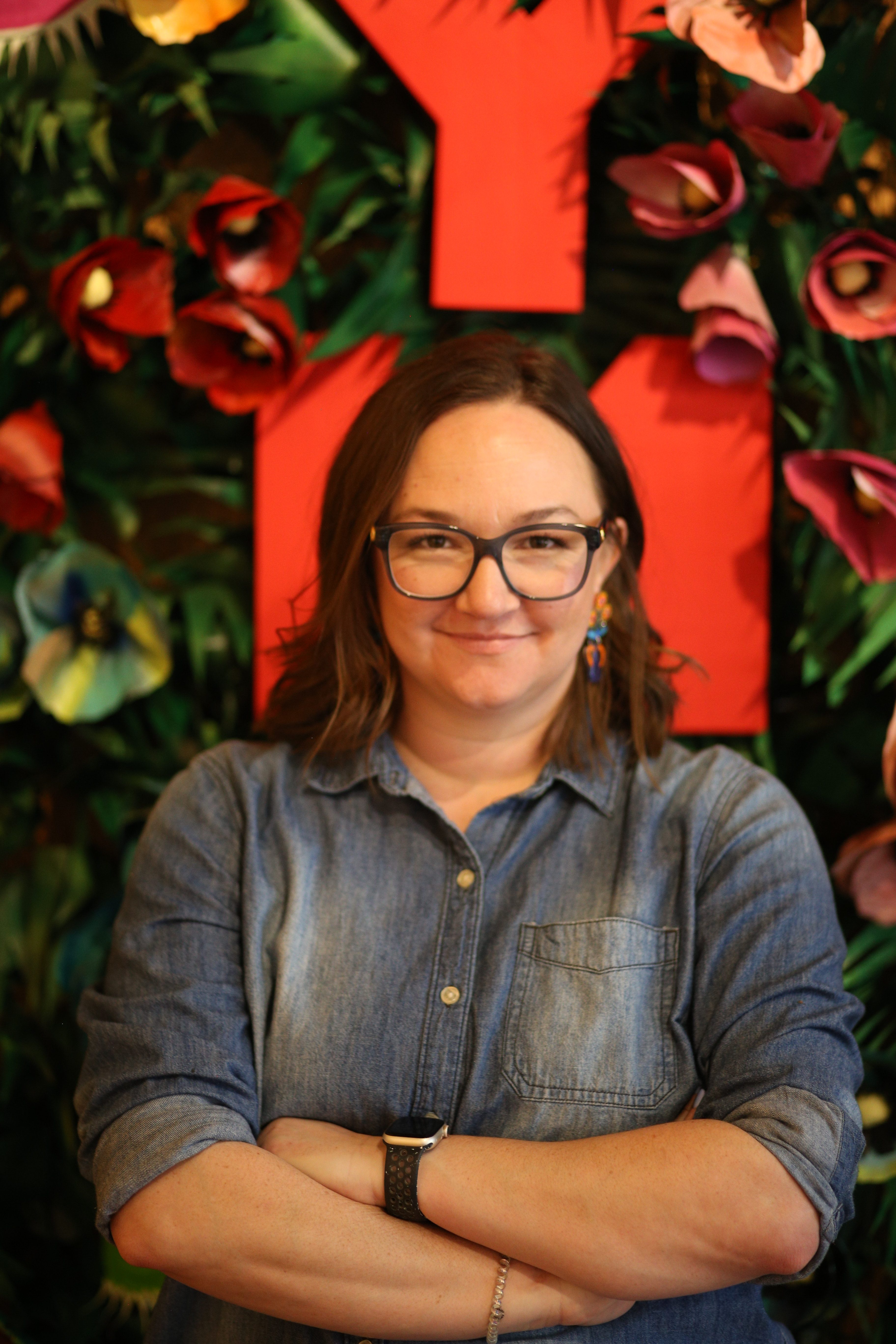 Portrait of artist Sam McCoy, smiling and standing in front of one of her vibrant illustrations.